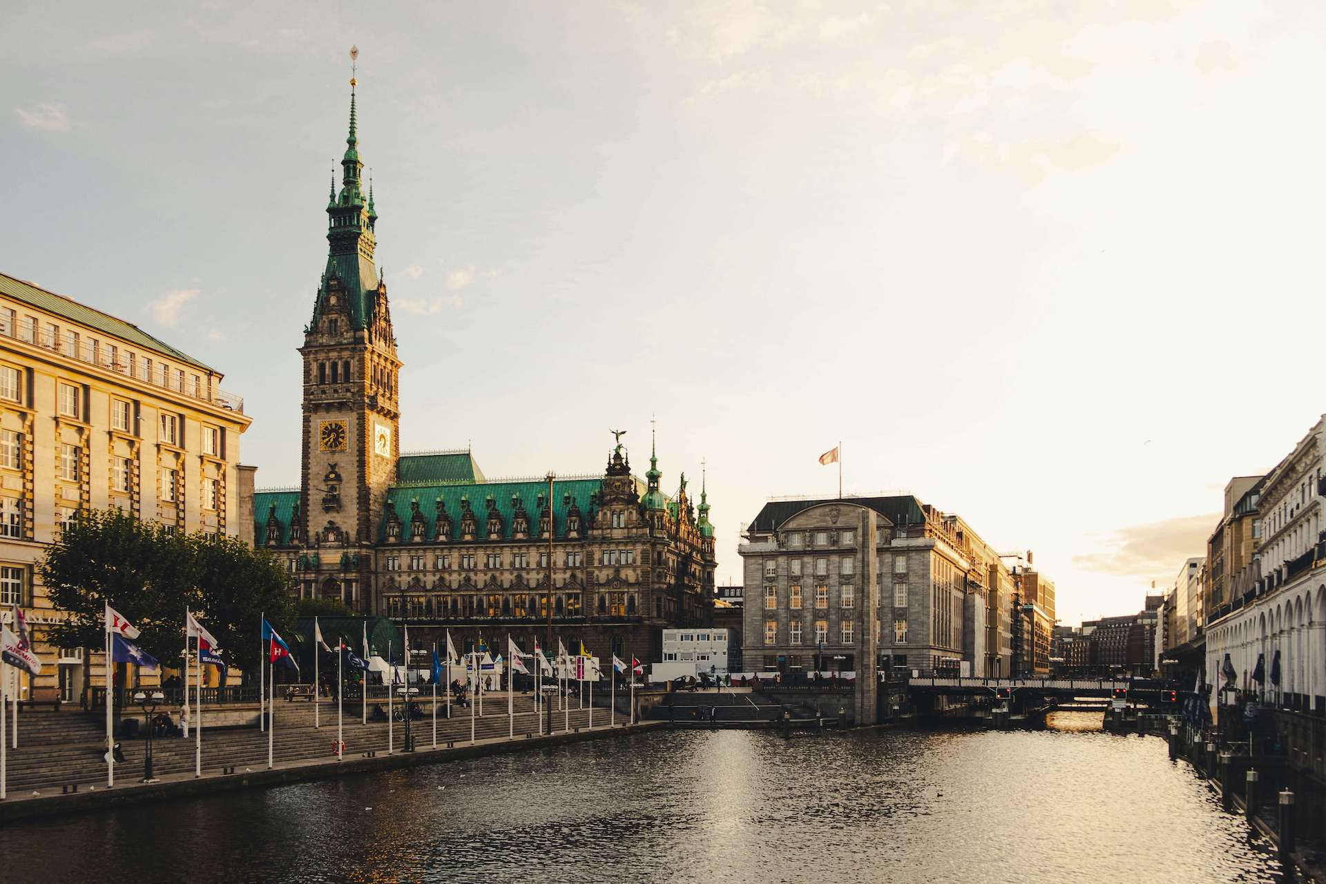 Historisches Gebäude mit Turm und Wasser im Vordergrund in einer Stadtlandschaft bei Sonnenuntergang.